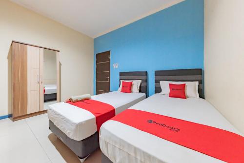 una camera con due letti con lenzuola rosse e bianche di RedDoorz Syariah @ Pangeran Suryanata Samarinda a Samarinda