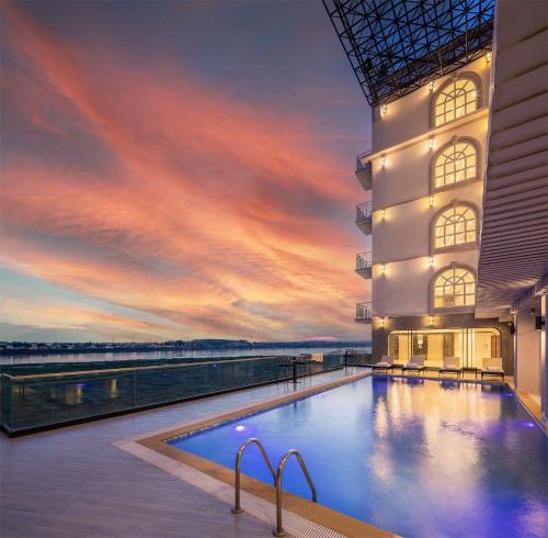 a swimming pool in front of a building with a sunset at Eastin Hotel Vientiane in Vientiane