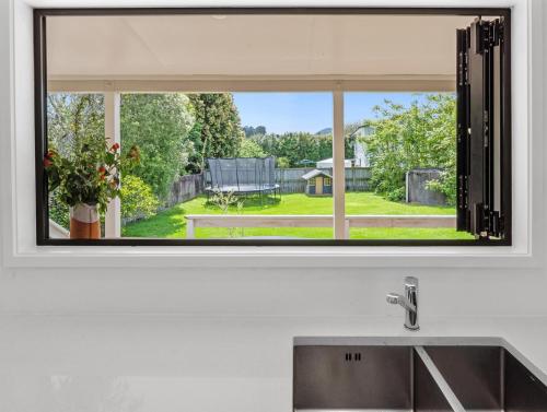 Omaha的住宿－Waimanu Bliss Escape - Point Wells Holiday Home，厨房里设有水槽上的窗户,享有庭院的景色