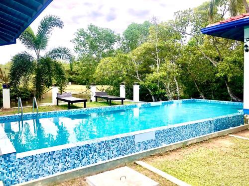 a blue swimming pool with two picnic tables and trees at Seth Villa by Magampura Resorts in Tangalle