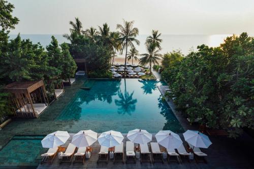 a swimming pool with chairs and umbrellas next to the ocean at Cape Nidhra Hotel in Hua Hin
