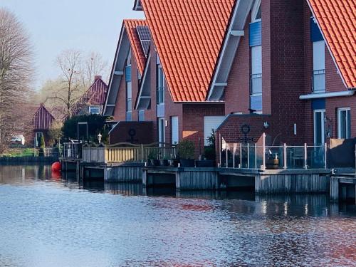 una casa con techos rojos junto a un cuerpo de agua en Ferienwohnung Seegang 25493, en Weener