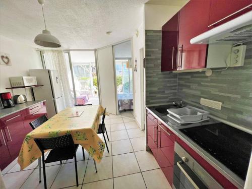 La cuisine est équipée d'une table, d'un évier et de placards rouges. dans l'établissement Charmant T2 avec belle terrasse expo Sud, parking privé, proche plage et commerces - FR-1-307-187, au Grau-du-Roi