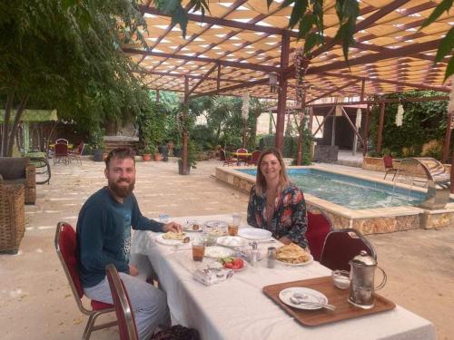 un hombre y una mujer sentados en una mesa frente a una piscina en Green house en Ajloun