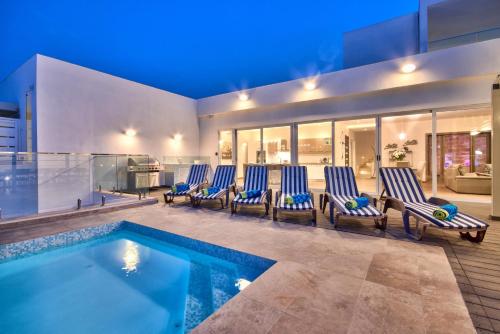 una casa con una piscina con sillas azules en Maltese Luxury Villas - Sunset Infinity Pools, Indoor Heated Pools and More!, en Mellieħa