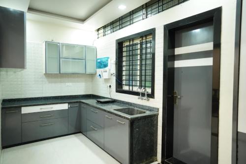 cocina con armarios grises, fregadero y ventana en Kantesha Nest en Shimoga