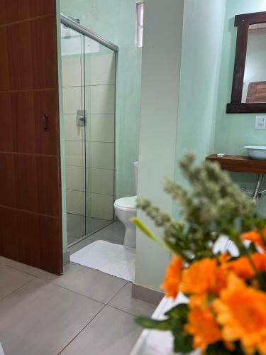 ein Bad mit einer Dusche, einem WC und einer Vase aus Blumen in der Unterkunft Pousada Certa Express in Chapada dos Guimarães