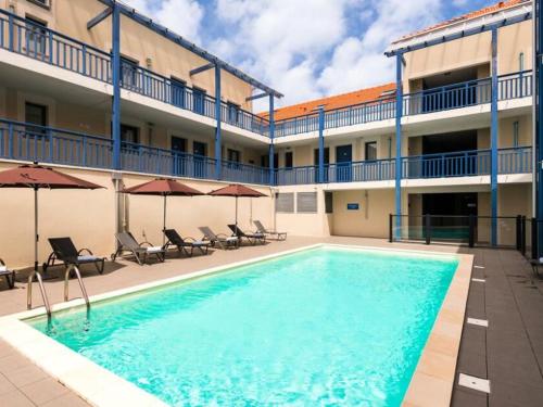 une piscine devant un hôtel avec chaises et parasols dans l'établissement Appartement T2 avec piscine, proche océan, linge et ménage inclus, à Biscarrosse Plage - FR-1-319-455, à Biscarrosse