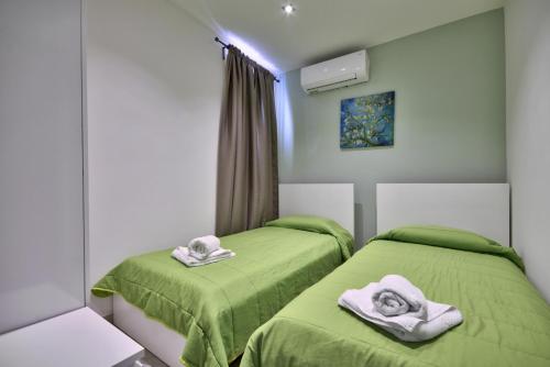 duas camas num quarto com lençóis verdes e toalhas em CityVista - Gzira Apartments and Penthouse by ShortletsMalta em Il-Gżira