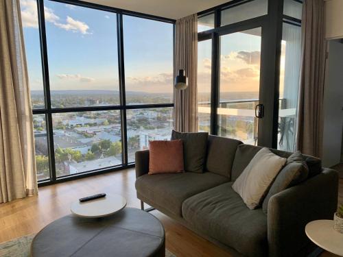 a living room with a couch and large windows at CBD Stunning TOP Floor View - FREE Parking FREE Netflix FREE Gym FREE Pool FREE Sauna FREE BBQ Area FREE Coffee in Adelaide