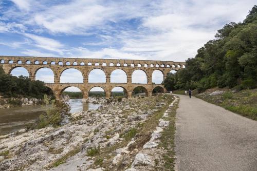 a bridge over a river with a person walking down a road at Residhotel Résidence Pont du Gard in Remoulins