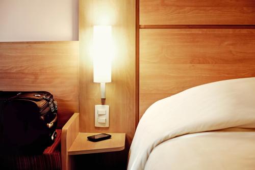 a hotel room with a bed and a light on the wall at ibis Marseille Provence Aéroport in Marignane