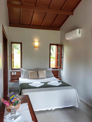 a bedroom with a bed and a table and two windows at Pousada Recanto da Grande Paz in Alto Paraíso de Goiás