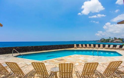 a pool with chairs and the ocean in the background at Unobstructed ocean views, Oceanside Pool, 2B/2B, Sleeps 6 in Kailua-Kona