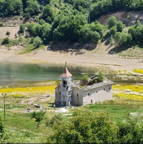 an old building in a field next to a body of water at Mavrovo Square " Villas & Apartment " in Mavrovo