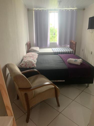 two beds in a room with a chair and a window at Pousada Recanto do Mar in Saquarema