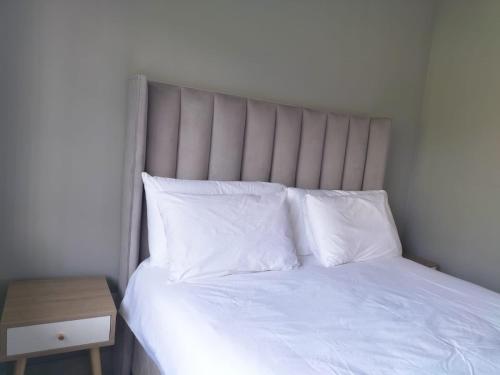 a bed with white sheets and pillows next to a table at Vic's place - With backup power in Sandton