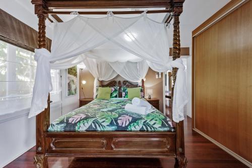 Airlie Getaway - Airlie Beach في شاطئ إيرلي: غرفة نوم مع سرير المظلة مع الوسائد الخضراء