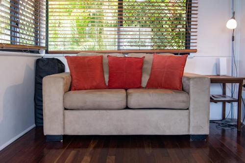 a couch with four red pillows on it in a room at Airlie Getaway - Airlie Beach in Airlie Beach