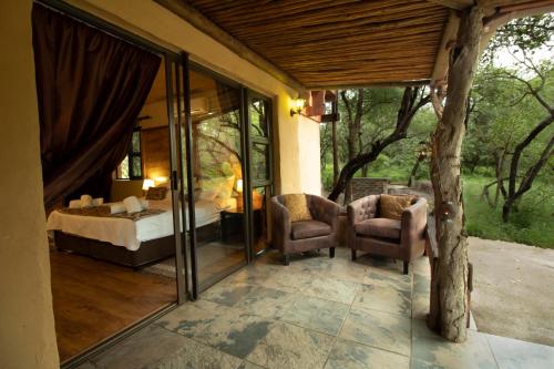 a bedroom with a bed and two chairs on a patio at Adventure Bush Villa in Marloth Park