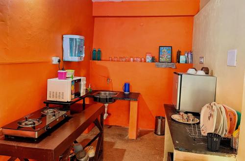 a kitchen with orange walls and a stove and a microwave at Sandev Homestay in Madikeri