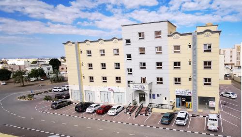 ein großes weißes Gebäude mit Autos auf einem Parkplatz in der Unterkunft Sama Sohar Hotel Apartments - سما صحار للشقق الفندقية in Suhar