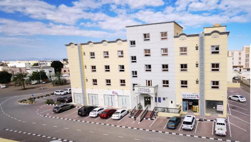 a large white building with cars parked in a parking lot at Sama Sohar Hotel Apartments - سما صحار للشقق الفندقية in Sohar