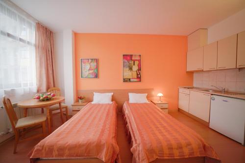 two beds in a room with a table and a kitchen at Apartments Flora-Daisy in Borovets
