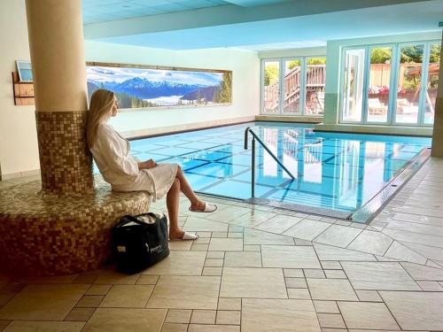 a woman sitting on a chair next to a swimming pool at Superior Sport und Familienresort Alpenblick in Zell am See