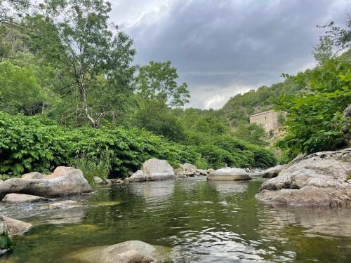 a river with rocks and a building in the background at Votre gite dans l'ancienne Huilerie de Tourtel in Vernosc-lès-Annonay