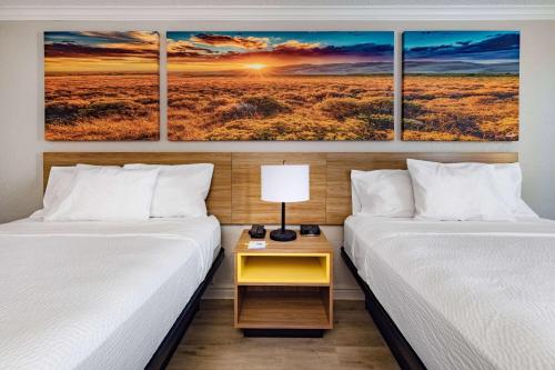 two beds in a room with three paintings on the wall at Days Inn by Wyndham Del Rio in Del Rio