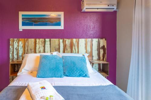 a bed with blue pillows and a purple wall at Pousada Flor de Lotus in Praia do Rosa