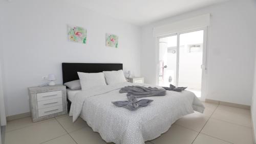 ein weißes Schlafzimmer mit einem Bett mit einer Blume darauf in der Unterkunft REF 9959 Green Apartment La Marina in Elche