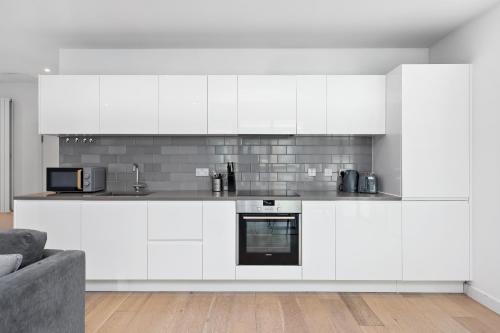 a white kitchen with white cabinets and a couch at Cave Apartments in London