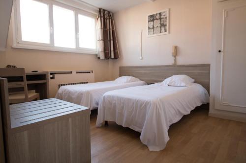 a room with two beds and a desk and a window at Hôtel Pacific in Calais