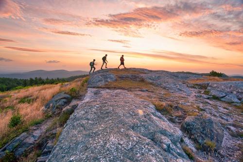 three people walking on the top of a mountain at sunset at CoHo: Conway Hostel in Conway