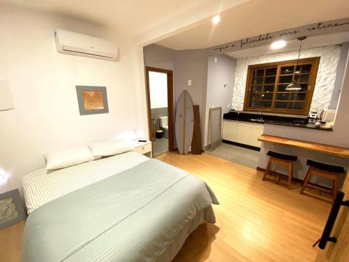 a bedroom with a bed and a desk and a kitchen at Studios Aromas do Campeche - Floripa in Florianópolis