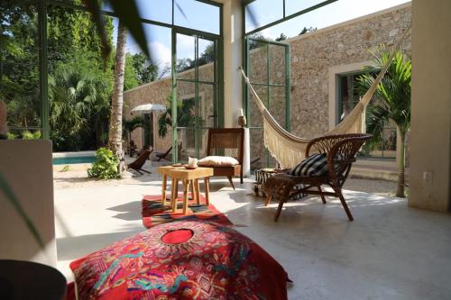 un porche con hamaca y sillas y una habitación con ventanas en Nuik Casa Tropical en Mérida