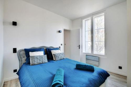 a bedroom with a blue bed with two windows at Appartement aux Portes de Paris in Saint-Denis