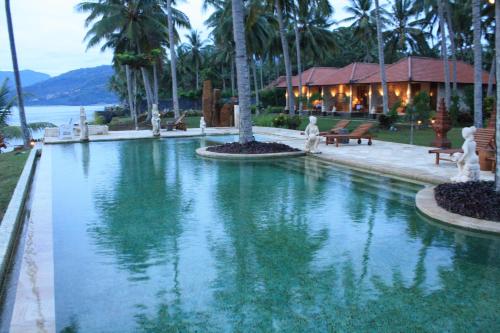 a pool of water with palm trees and a building at Sea Breeze Candidasa in Candidasa