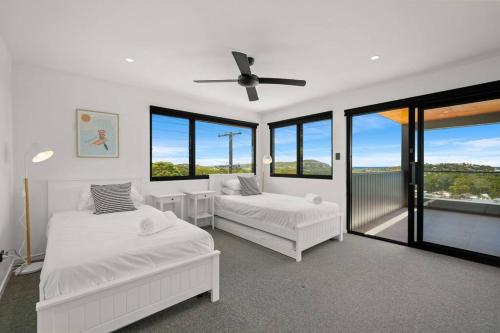 1 dormitorio blanco con 2 camas y ventanas en Luxe Terrigal beach Ocean View with Infinity pool en Wamberal