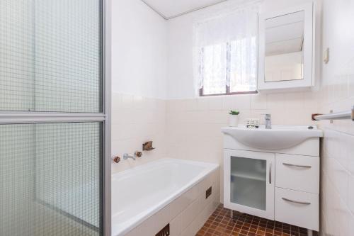 La salle de bains blanche est pourvue d'un lavabo et d'une douche. dans l'établissement Carinya Gardens 15, à Forster