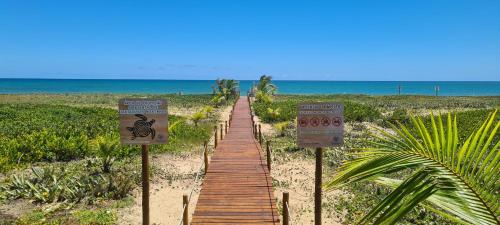 a wooden path leading to the beach with signs at Bangalô Tavarua Itacimirim Pé na areia in Itacimirim