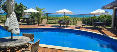 a swimming pool with a table and chairs and the ocean at Bangalô Tavarua Itacimirim Pé na areia in Itacimirim