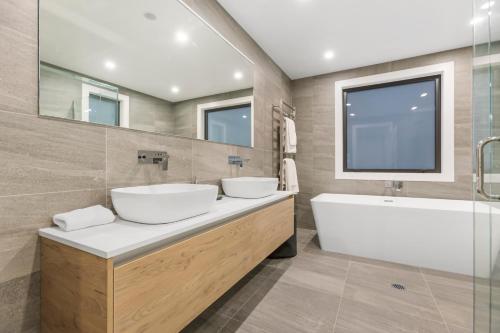 La salle de bains est pourvue de 2 lavabos, d'une baignoire et d'une grande fenêtre. dans l'établissement The Rocks Apartment, à Wanaka