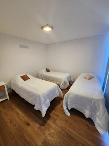1 dormitorio con 2 camas, sábanas blancas y suelo de madera. en Cabañas Manzana 21 en Mar del Plata