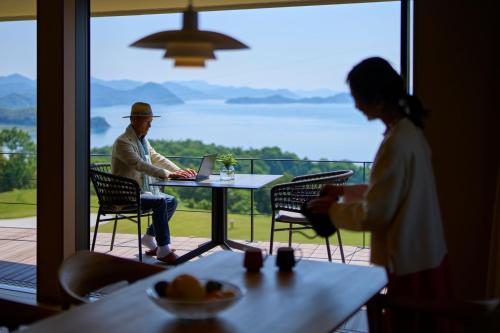 a man and a woman sitting at a table with a laptop at 瀬戸内ゴルフリゾートヴィラ in Takekara