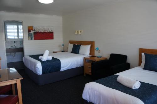 a hotel room with two beds and a chair at Waves Motel and Apartments in Warrnambool