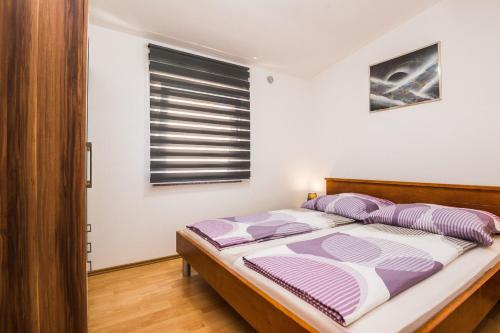 sypialnia z łóżkiem z fioletowymi poduszkami i oknem w obiekcie Apartments Skundric w mieście Vir