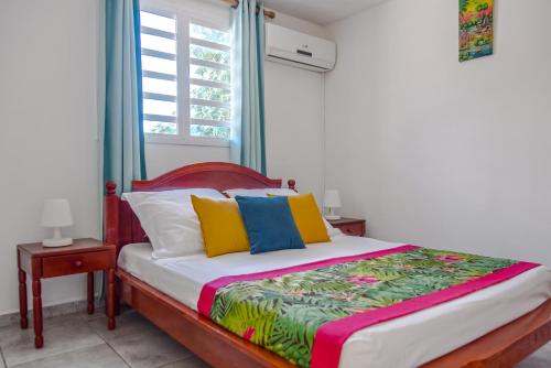 a bed with colorful pillows in a room with a window at Les Hauts de Sainte-Anne "2 Spas privatifs" in Sainte-Anne